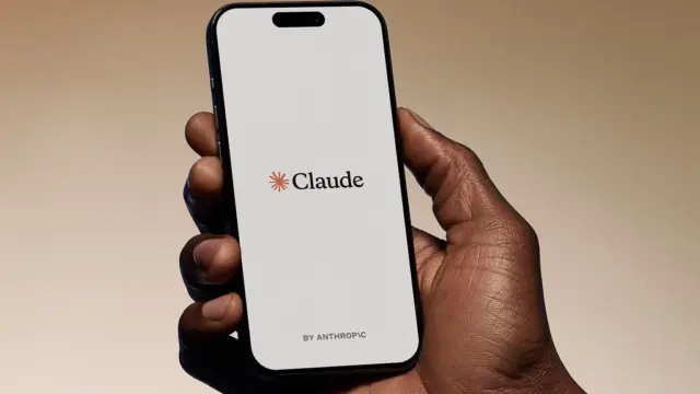 טלפון עם הלוגו של Claude מבית Anthropic על מסך לבן, מוחזק ביד על רקע חם
