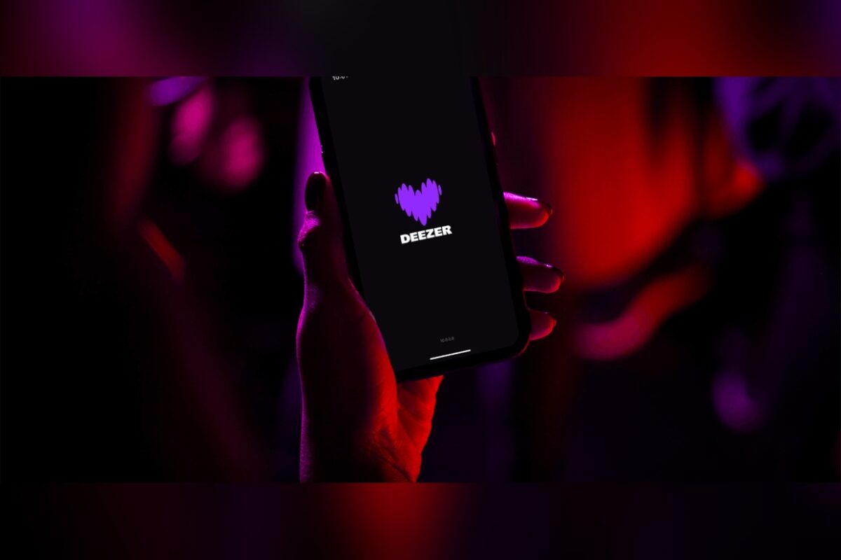 טלפון עם הלוגו של Deezer על המסך, ביד על רקע אדום-סגול חשוך