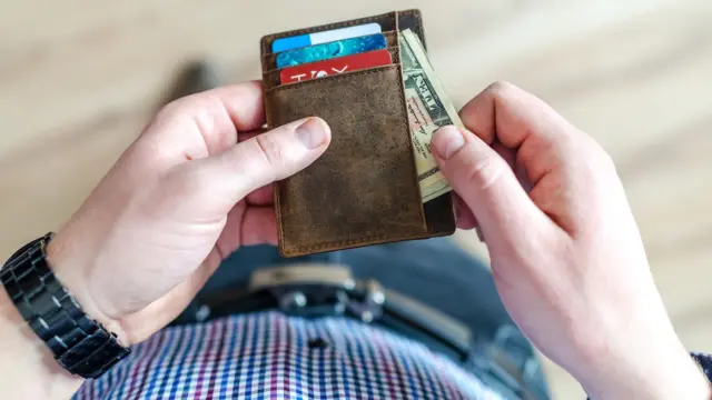ידיים של אדם מחזיקות ארנק עור חום עם כרטיסים ושטרות כסף, ללא פנים בתמונה